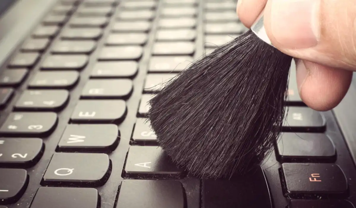 A male hand cleaning dirty computer keyboard with brush to remove dust