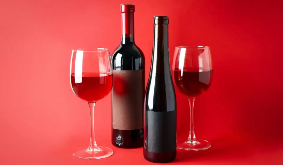 Bottles and glasses of wine on red background