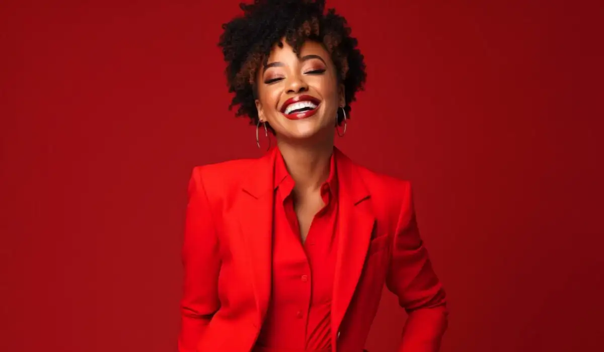 Black woman smiling and staring at camera while wearing red suit against red background
