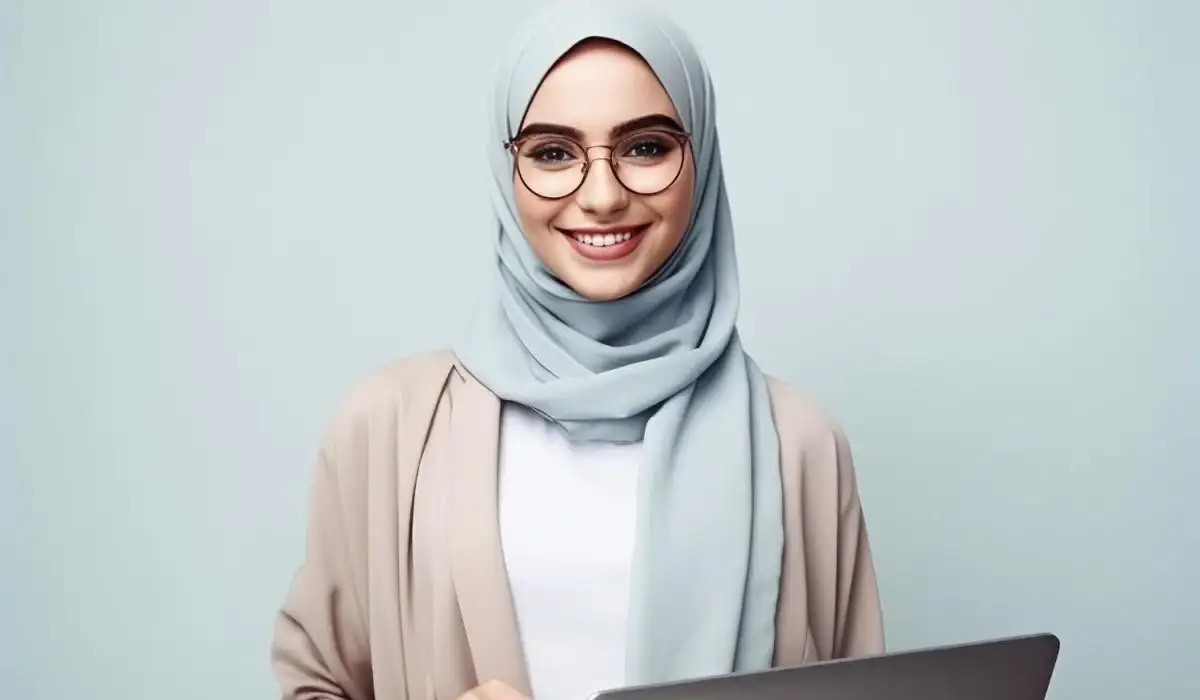 A woman in a hijab with glasses using a laptop.