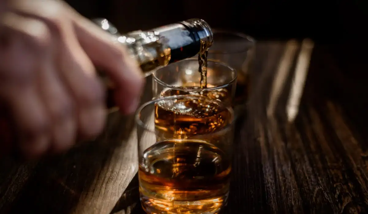Pour a strong alcoholic drink, be it whiskey, into the glasses that are on the wood.