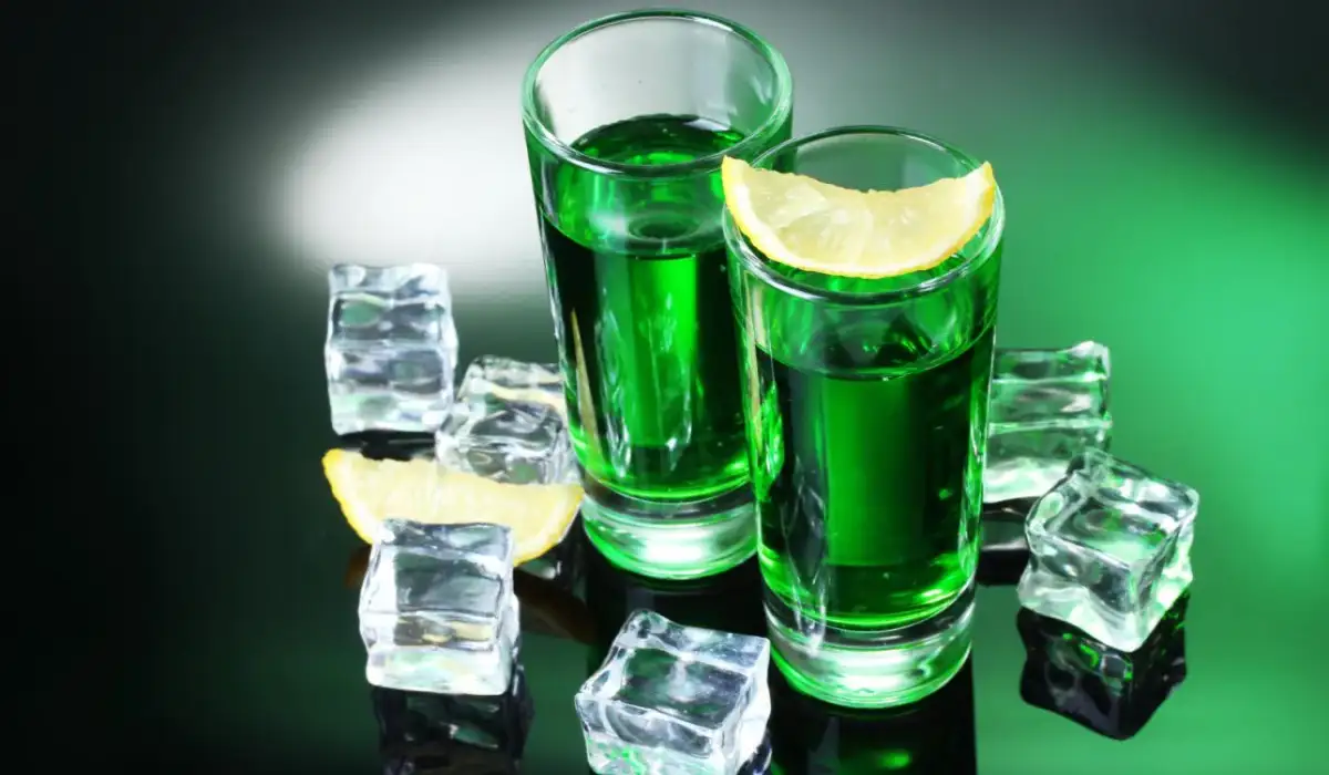 Two glasses of absinthe lemon and ice on green background
