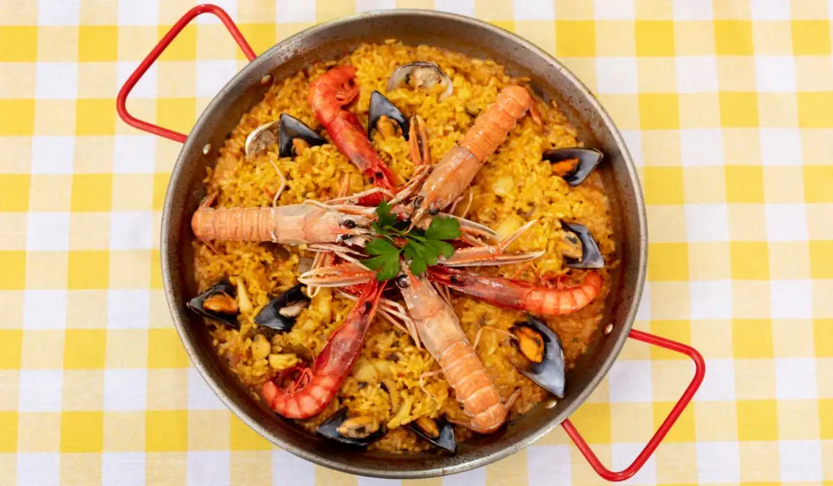 Delicious Spanish paella in a saucepan on a table with checkered mat