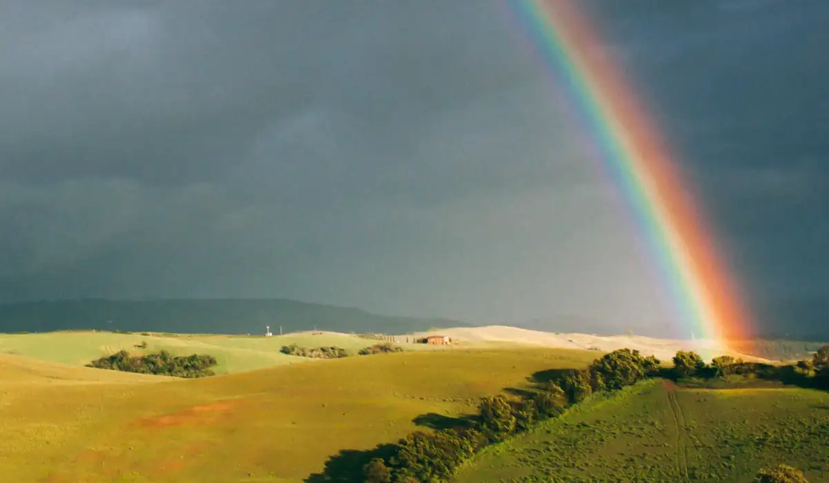 Bright rainbow and green hills on dark cloudy sky background