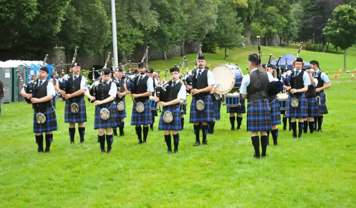 Several men playing the bagpipes outdoors in a formation with a bass drum