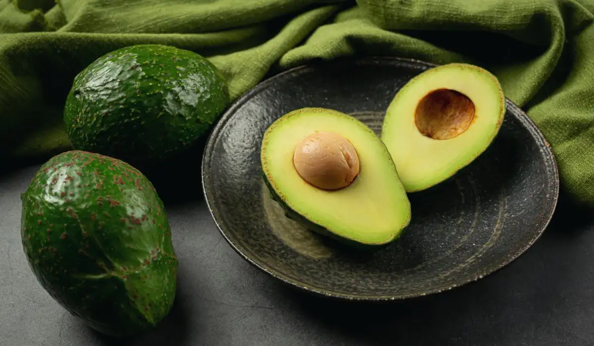 Three avocados, two on the table and one split on a plate