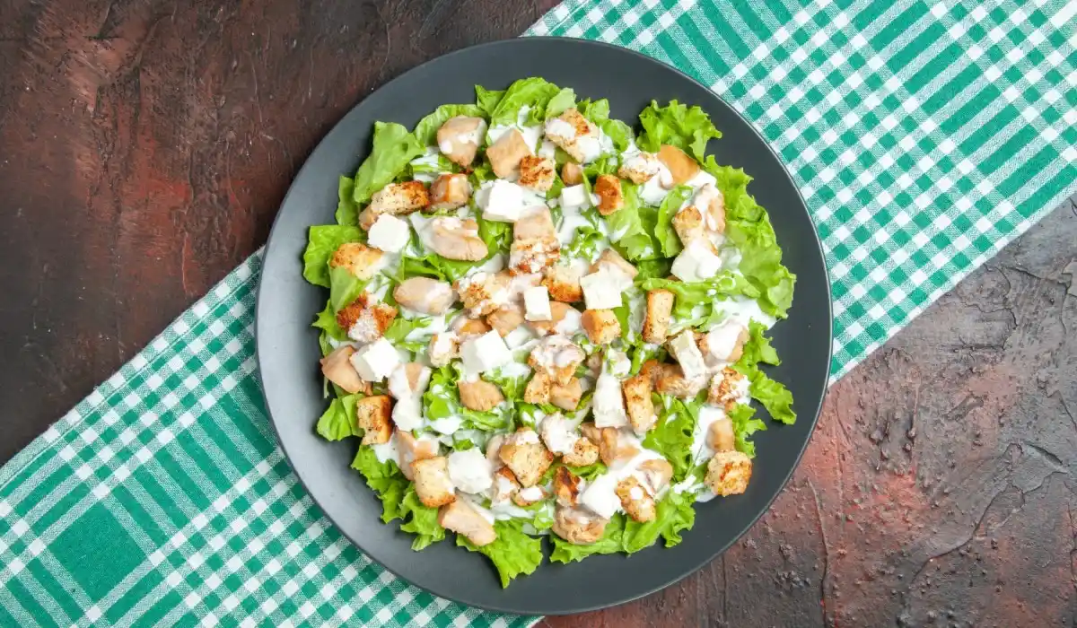Top view caesar salad on oval plate green white checkered tablecloth on dark table