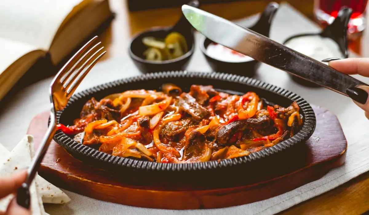 A person eating beef fajitas in a frying pan with cutlery