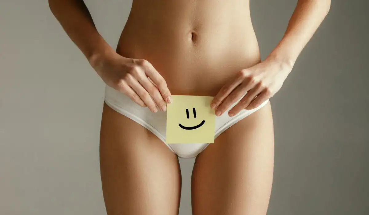 Female model holding card near stomach with paper sign or smile symbol on gray background.