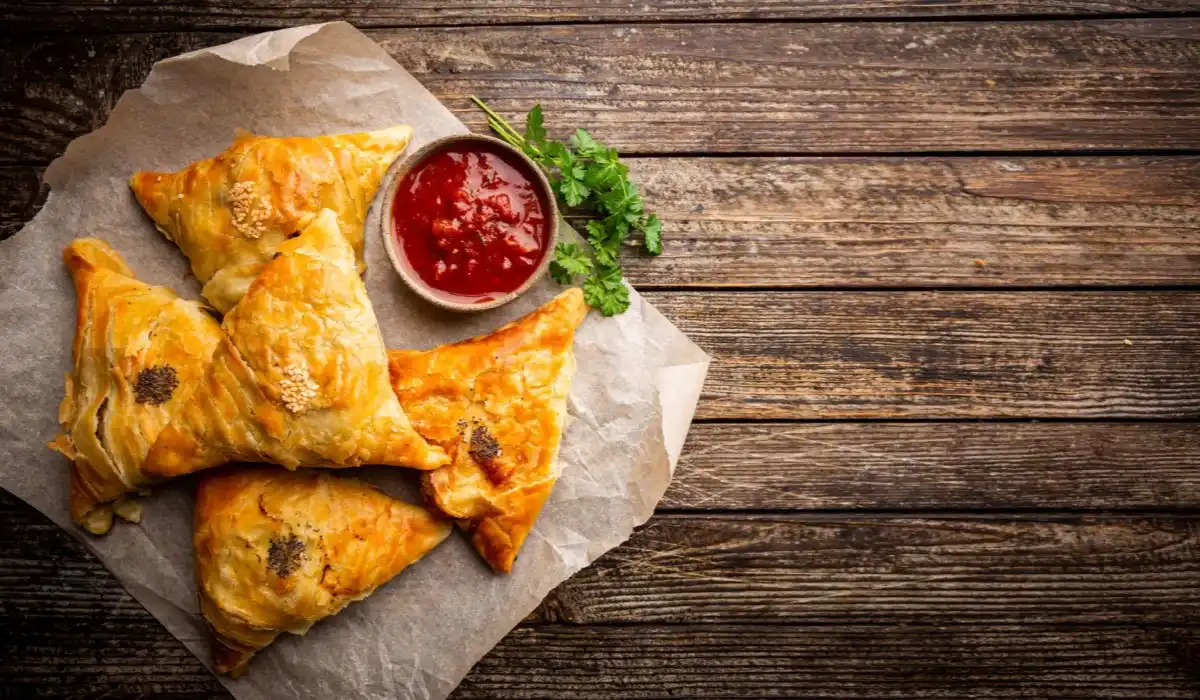 Samsa or samosas with meat and sauce on the side on wooden table