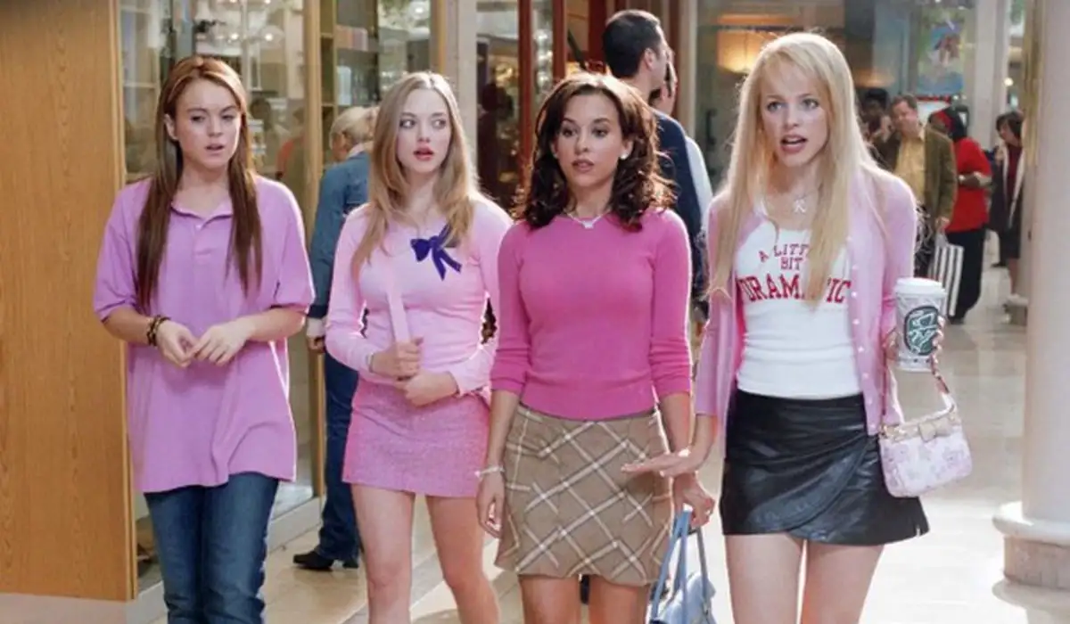 Cady, Karen, Regina and Gretchen characters from the movie Mean Girls walking on the street with several people and shops in the background