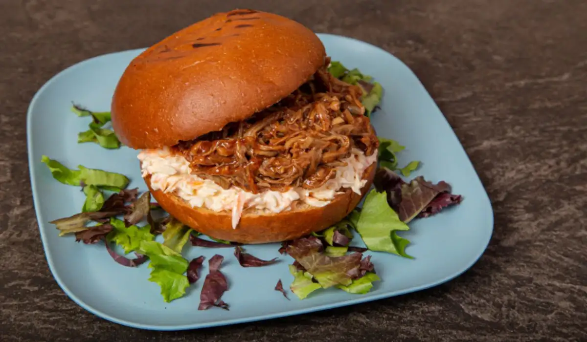 A juicy open pulled pork burger surrounded by vegetables on a blue plate