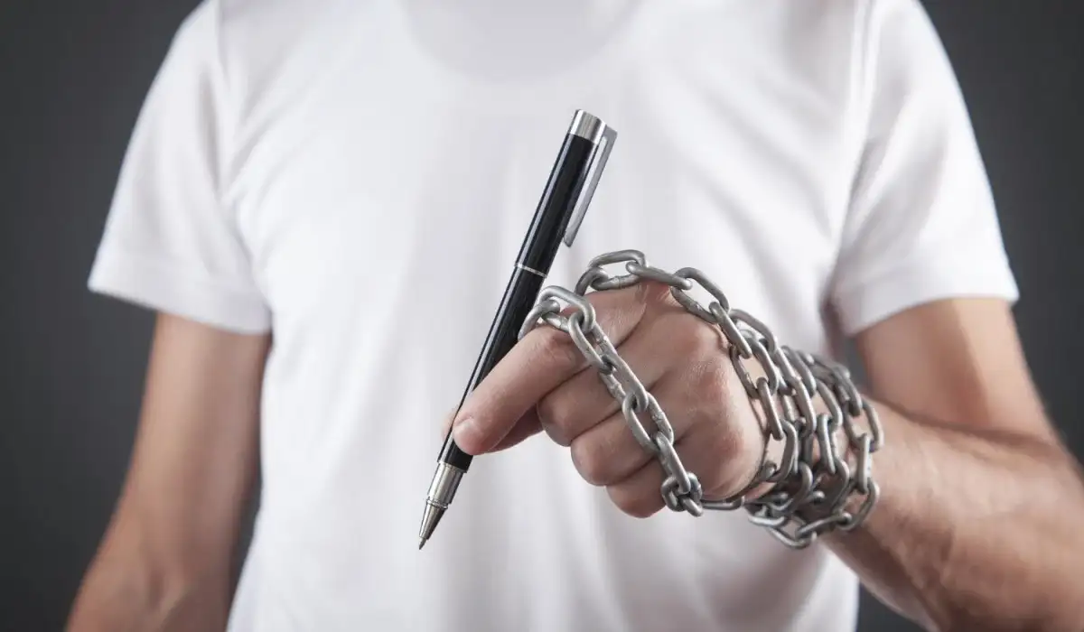 Hand of a journalist holding a pen tied with chains.