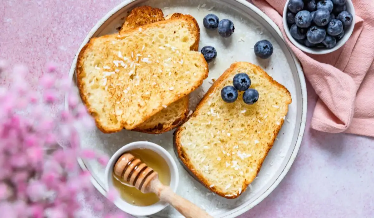French toast drizzled with honey and coconut flakes and blueberries on a handmade ceramic plate