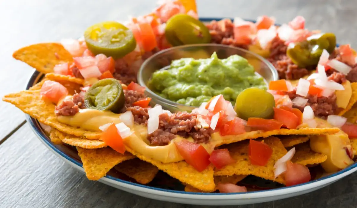 Mexican nachos with meat, guacamole, cheese sauce, peppers, tomato and onion on a plate on a wooden table