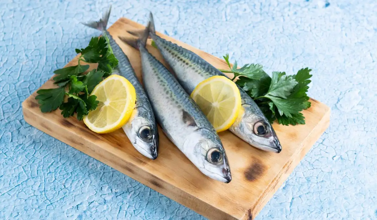 Three raw sardines with lemon slices on a board on a blue background