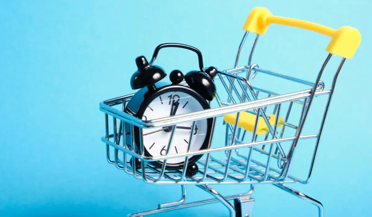 Alarm clock in miniature shopping trolley on blue background copy space