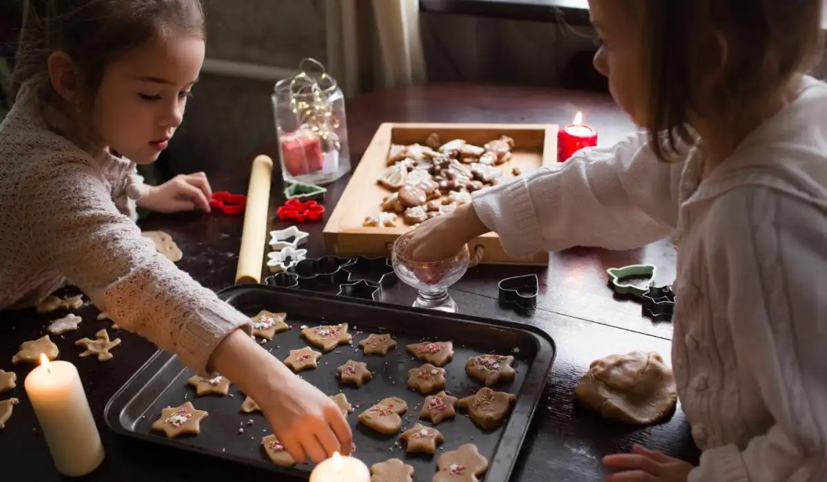 Lovely girls cook Christmas cookies together at home with candles on the table