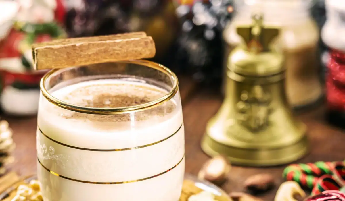 Winter drink called coquito decorated with cinnamon with a Christmas background and a bell
